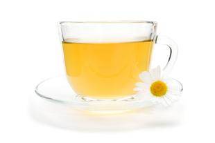Ein klarer Glasbecher, gefüllt mit einer gelblichen Flüssigkeit, begleitet von einer weißen Gänseblümchenblüte.