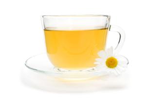 Ein klarer Glasbecher, gefüllt mit einer gelblichen Flüssigkeit, begleitet von einer weißen Gänseblümchenblüte.