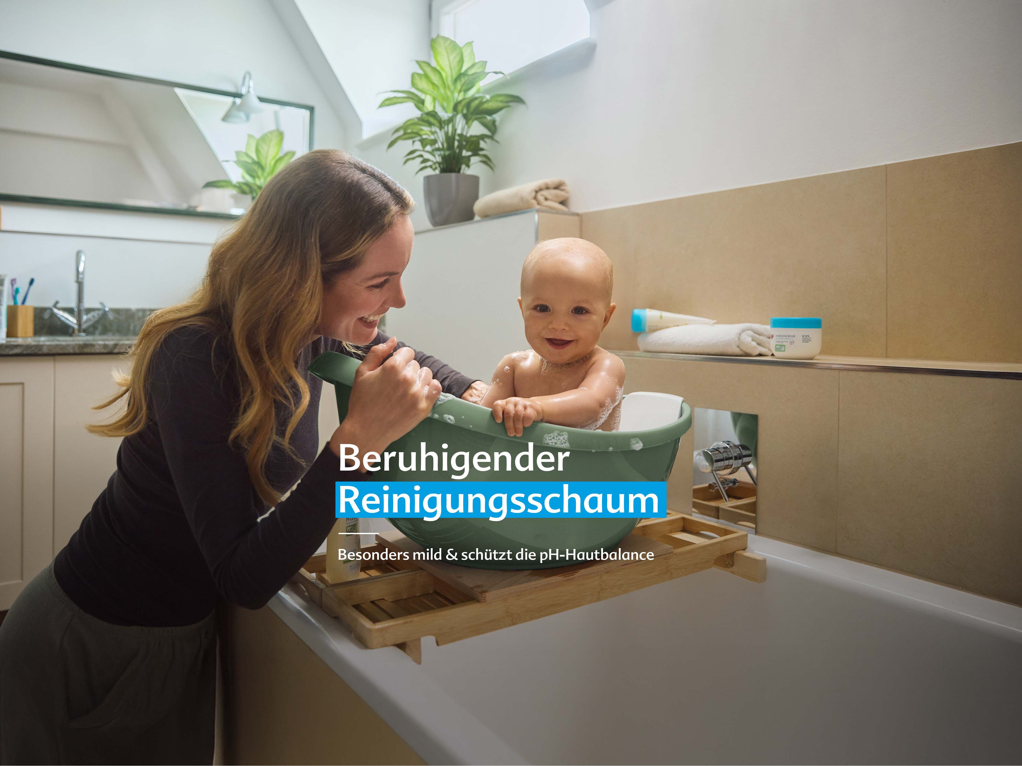 Mutter badet ihr lachendes Baby in einer kleinen Wanne mit sanftem Schaum, Text: „Beruhigender Reinigungsschaum – besonders mild & pH-hautneutral“.