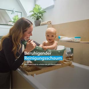 Mutter badet ihr lachendes Baby in einer kleinen Wanne mit sanftem Schaum, Text: „Beruhigender Reinigungsschaum – besonders mild & pH-hautneutral“.