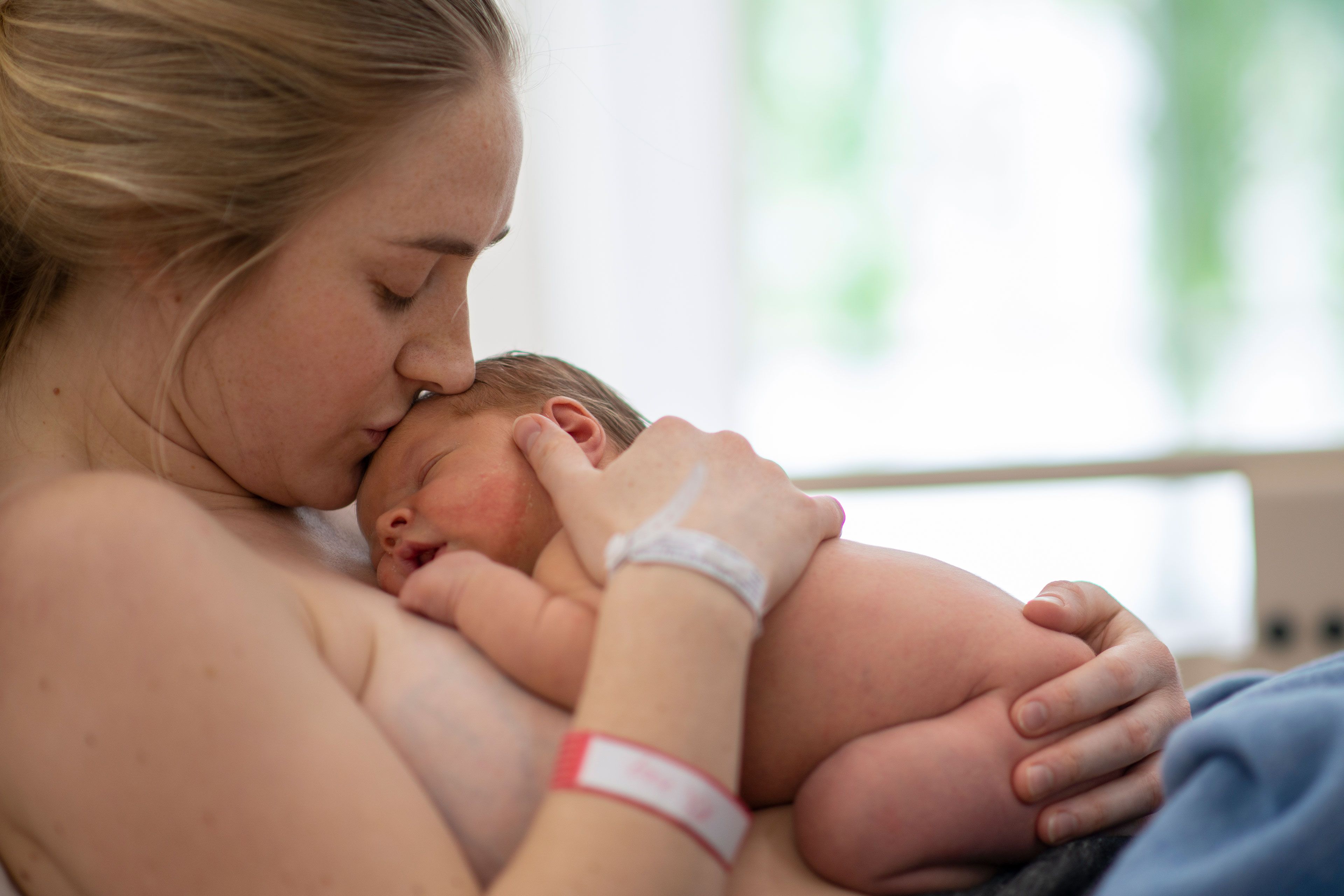 Ein zärtlicher Moment zwischen einer Mutter und ihrem neugeborenen Baby, wobei die Mutter sanft die Stirn des Babys küsst.