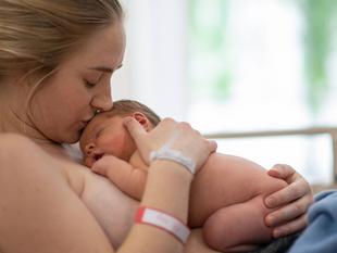 Ein zärtlicher Moment zwischen einer Mutter und ihrem neugeborenen Baby, wobei die Mutter sanft die Stirn des Babys küsst.