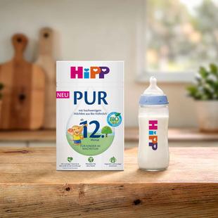 HiPP Kindermilch PUR Packung und gefülltes Fläschchen auf Holztisch in heller Küche, geeignet ab 12 Monaten