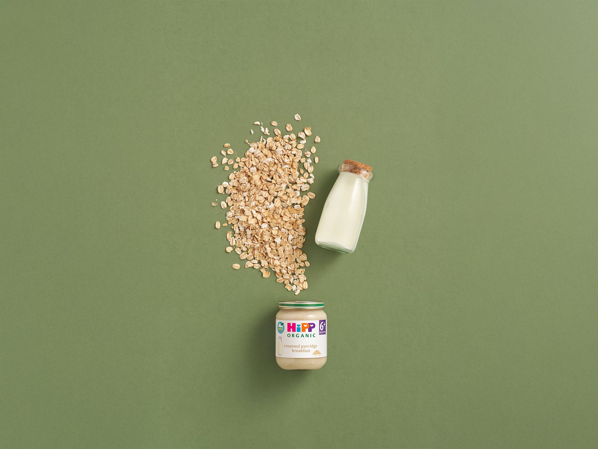 HiPP Organic Creamed Porridge Breakfast jar with oats and a bottle of milk on a green background