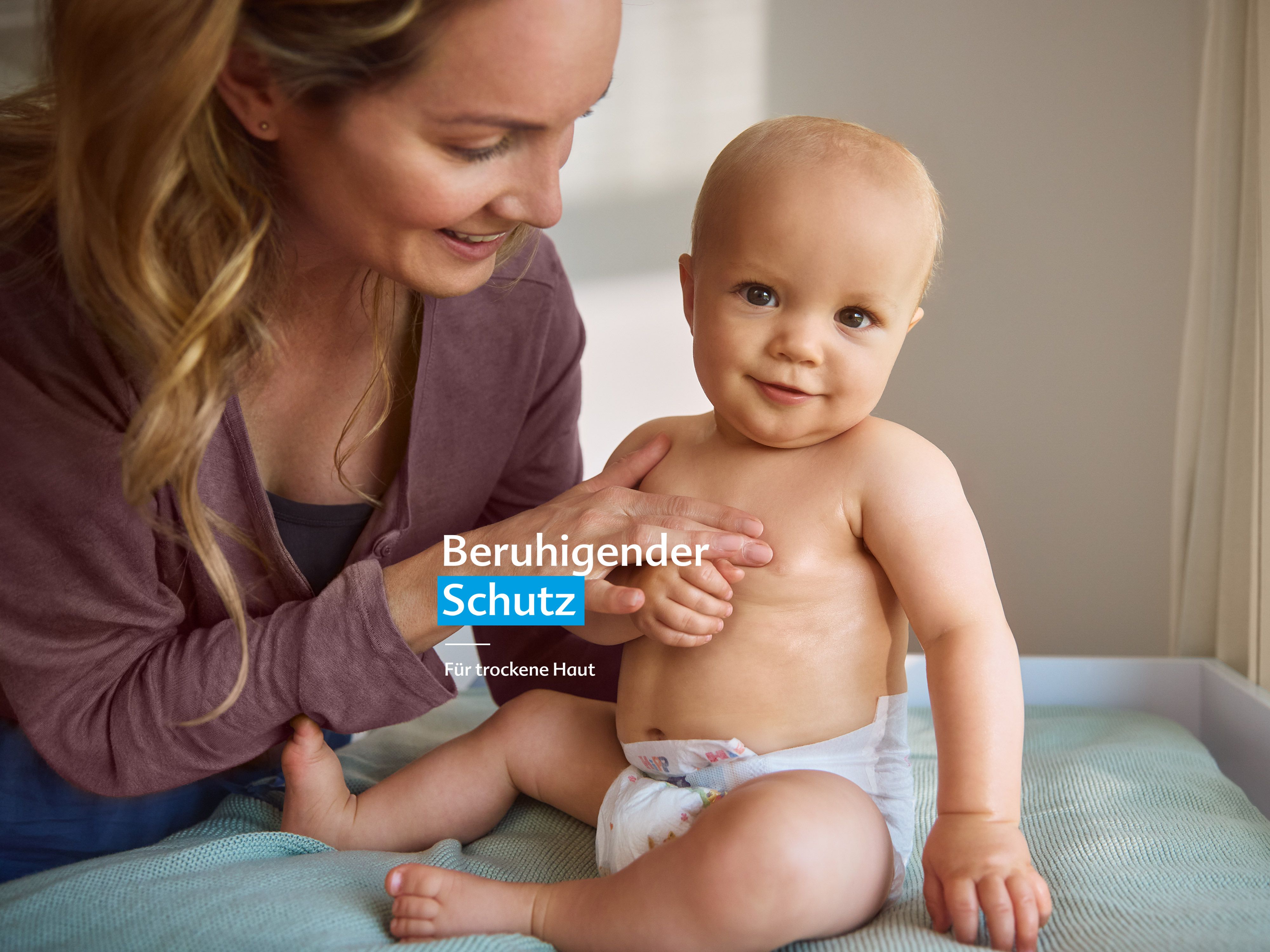 Mutter hält lächelnd Baby mit Windel auf Wickeltisch mit Text 'Beruhigender Schutz für trockene Haut'