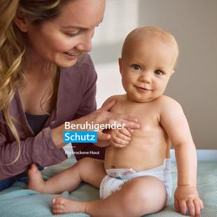 Mutter hält lächelnd Baby mit Windel auf Wickeltisch mit Text 'Beruhigender Schutz für trockene Haut'