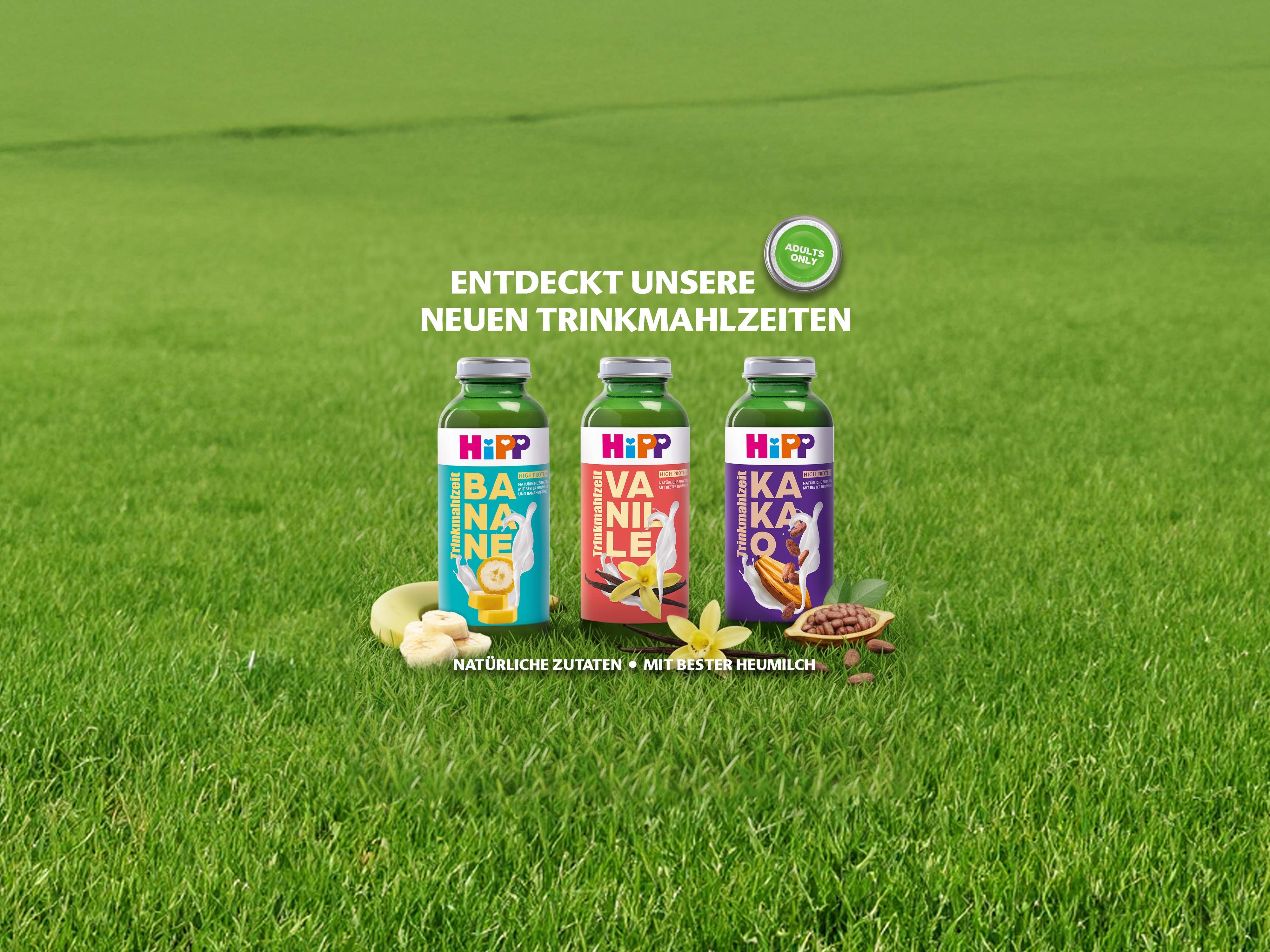 Drei Flaschen HiPP Trinkmahlzeiten mit den Geschmacksrichtungen Banane, Vanille und Kakao auf grünem Gras mit Text "Entdeckt unsere neuen Trinkmahlzeiten"