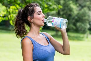 Eine Frau in einem blauen Tank-Top trinkt Wasser aus einer Flasche.