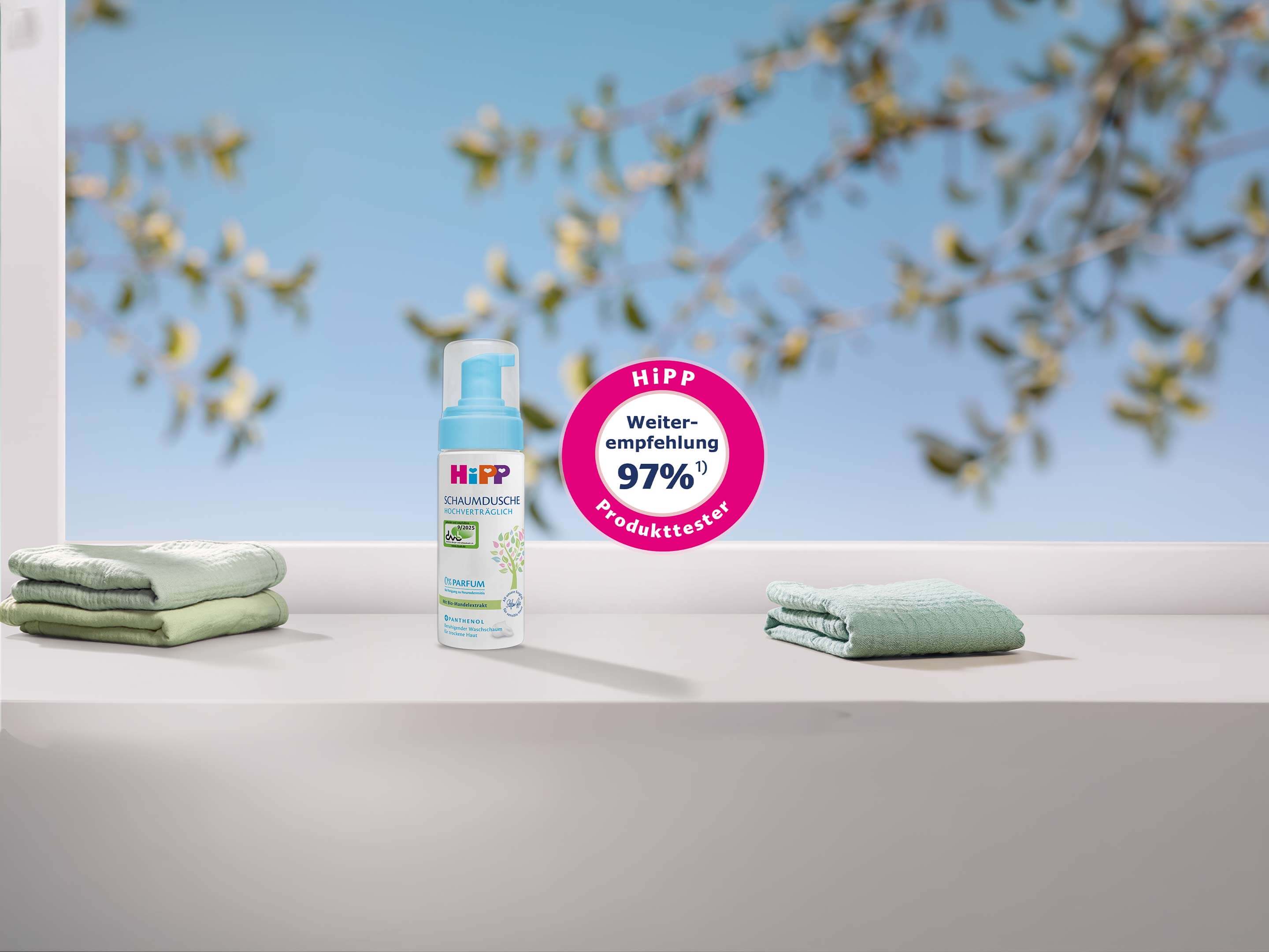 Flasche HiPP Babysanft Schaumdusche steht zwischen zwei gefalteten Handtüchern vor unscharfem Hintergrund 