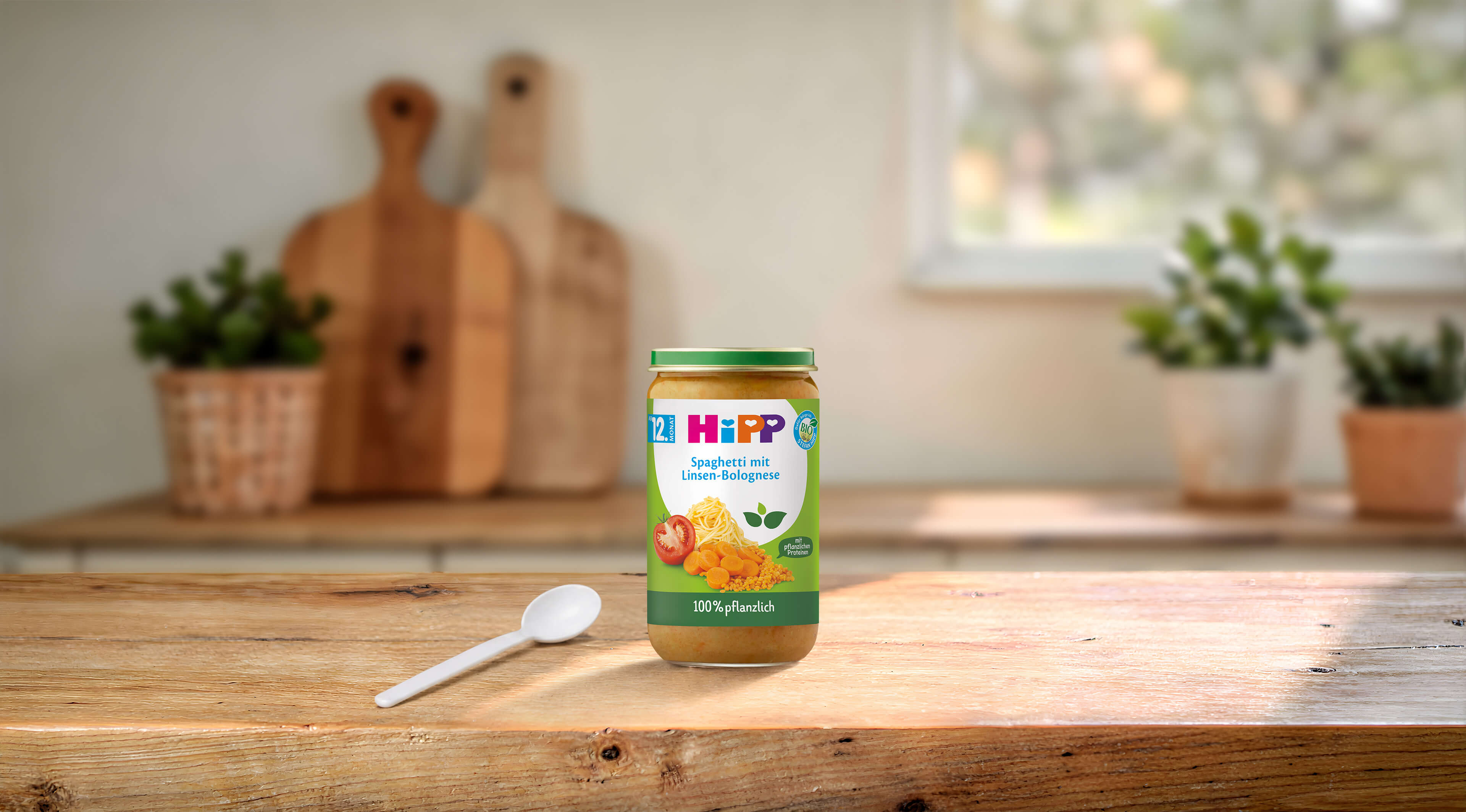 HiPP Bio Babyglas Spaghetti mit Linsen-Bolognese, 100 % pflanzliche Mahlzeit ab 12 Monaten auf Holztisch mit Löffel in Küche