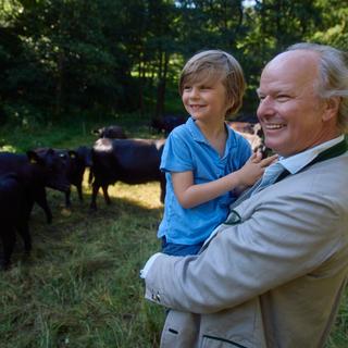 Stefan Hipp trägt seinen Sohn auf einem Feld zwischen Kühen