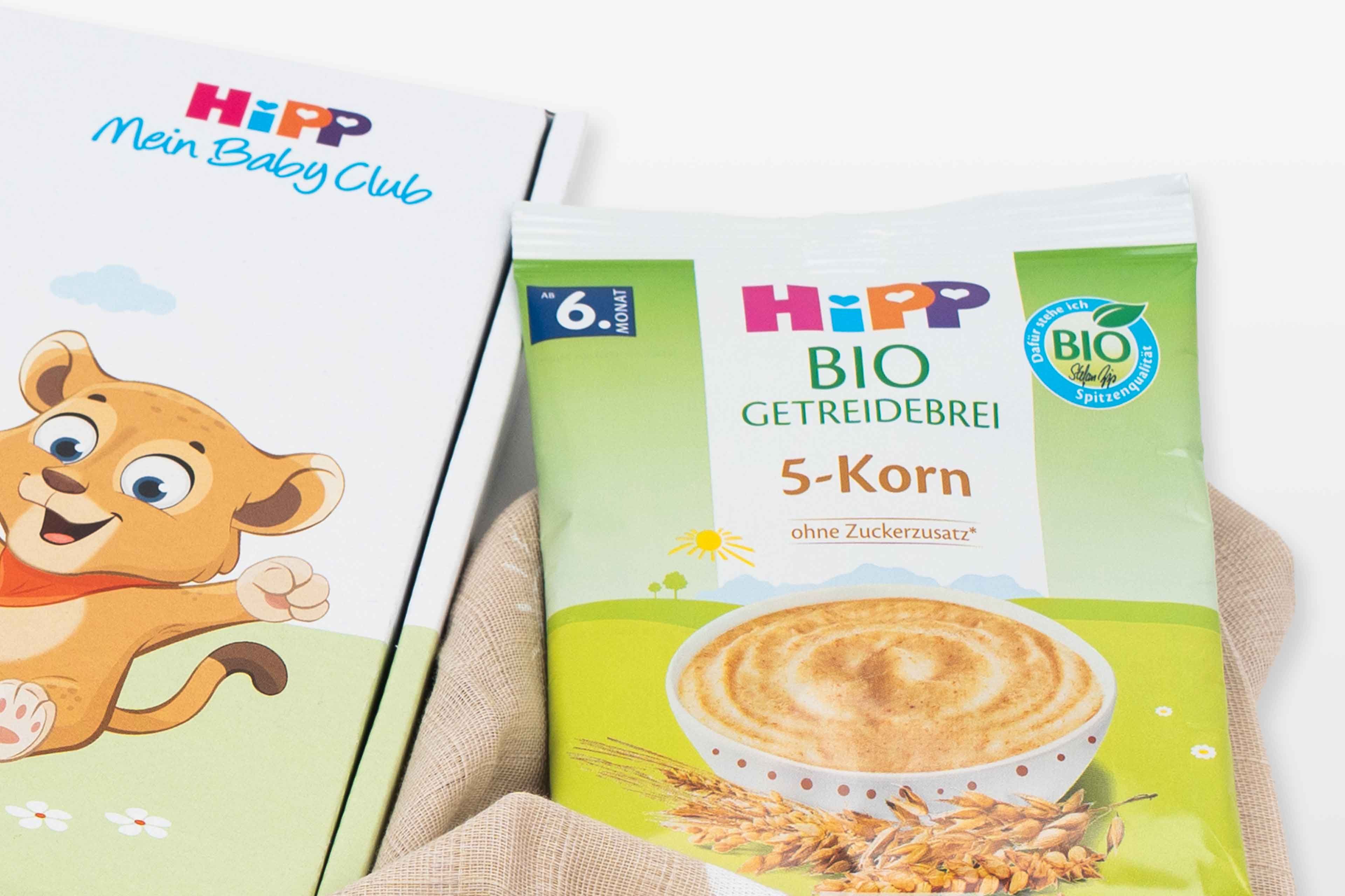 Verpackung von HiPP Bio-Getreidebrei Probebeutel 5-Korn neben HiPP Mein Baby Club-Box mit Löwenillustration