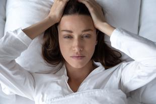 Eine auf einem Bett liegende Frau, die ihren Kopf mit beiden Händen hält und einen nachdenklichen Ausdruck zeigt.