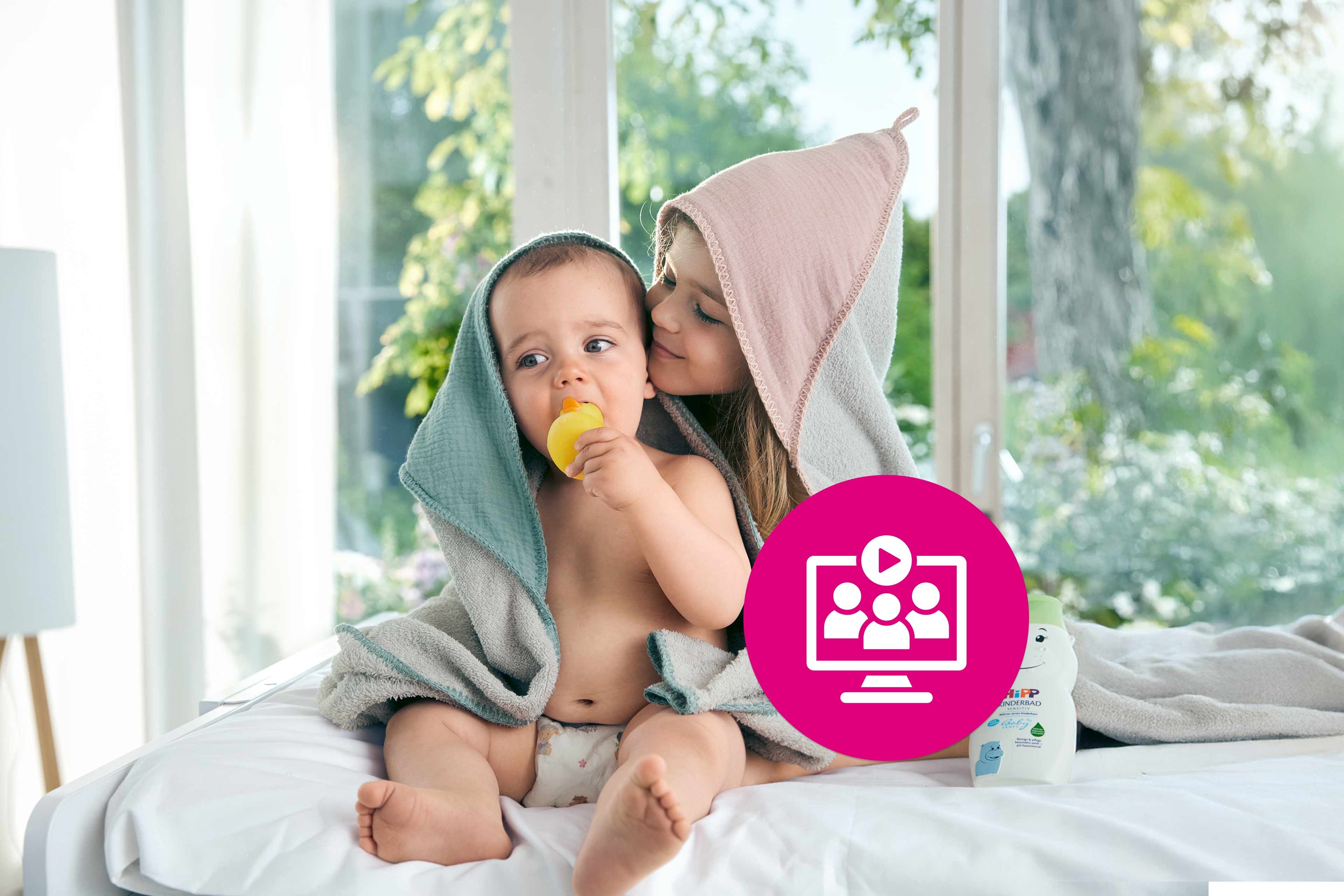 Baby und älteres Geschwister kuscheln nach dem Baden in Kapuzenhandtüchern, mit HiPP Pflegeprodukt und Webinar-Symbol im Vordergrund