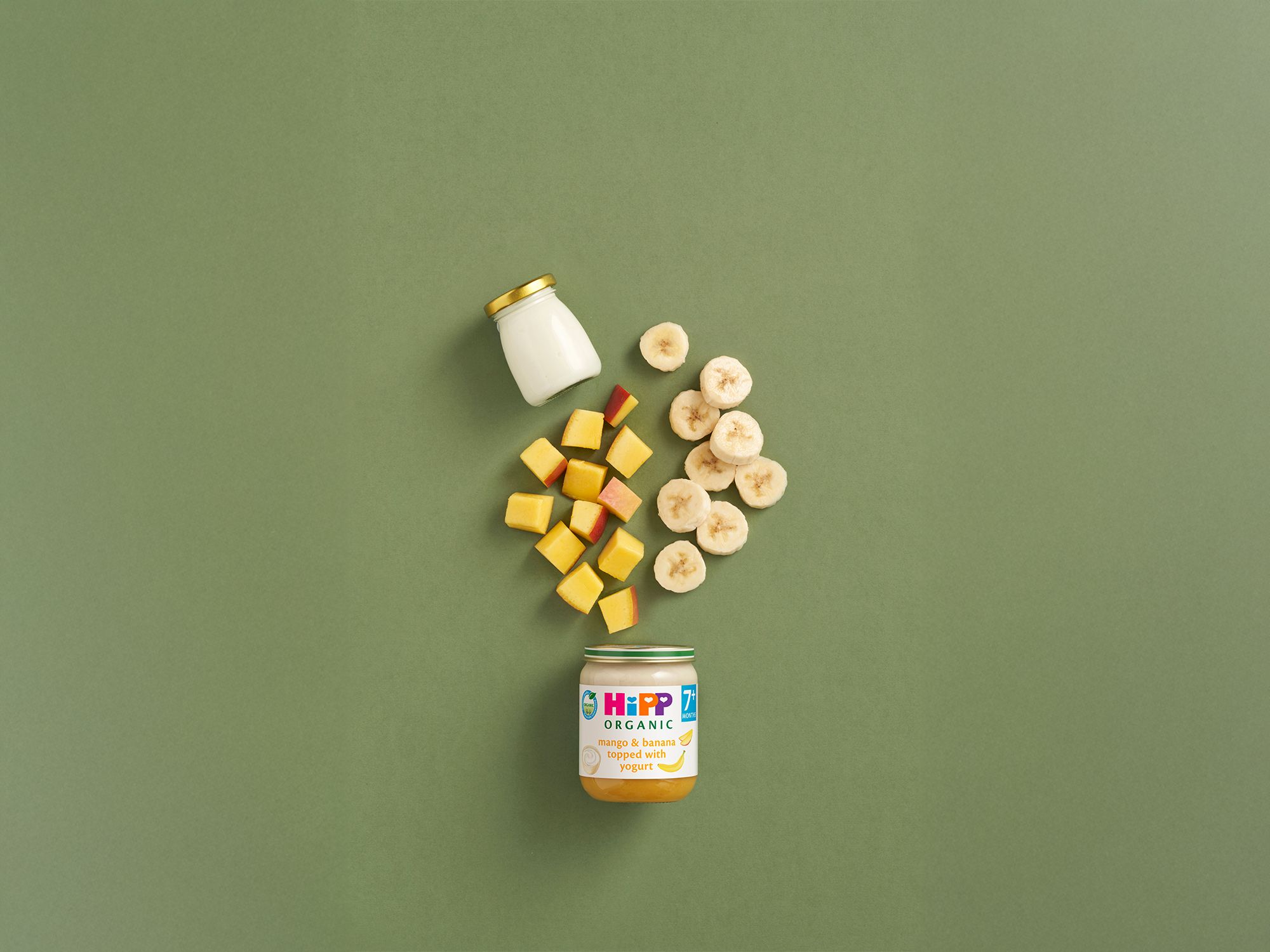 HiPP Organic Mango & Banana topped with Yoghurt jar with fresh banana slices, mango cubes and yogurt on a green background