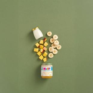 HiPP Organic Mango & Banana topped with Yoghurt jar with fresh banana slices, mango cubes and yogurt on a green background