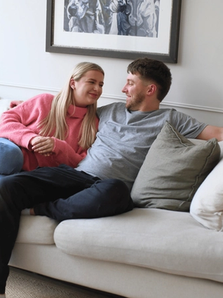 women and man sitting on a couch looking at each other and smiling.