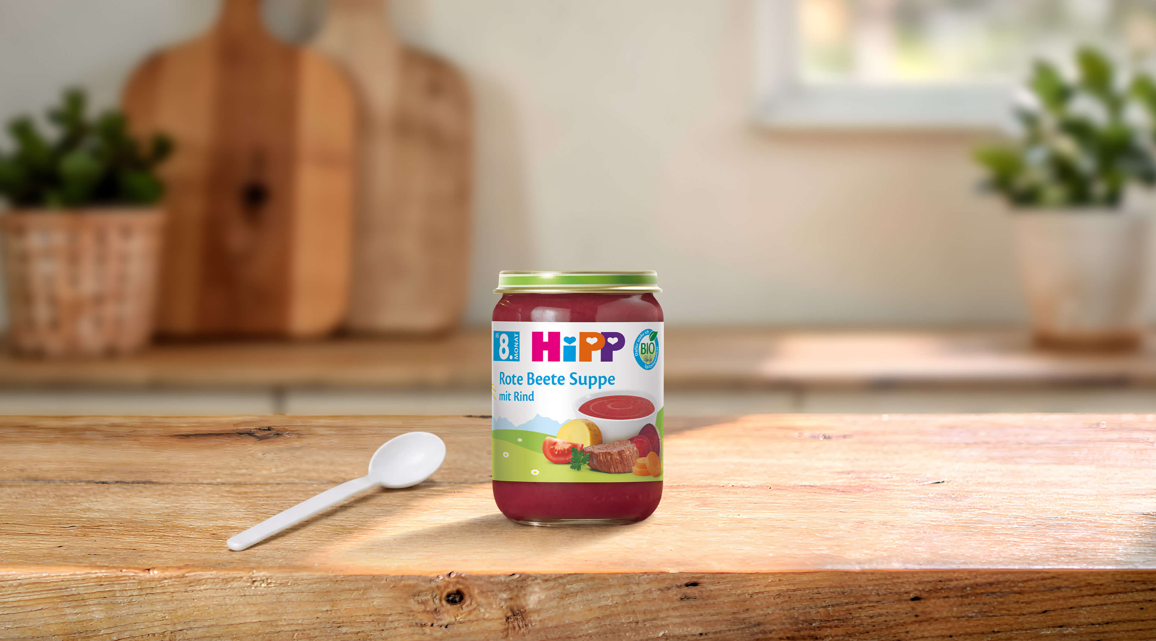 HiPP Bio Babyglas „Rote Beete Suppe mit Rind“ auf Holztisch mit Löffel in heller, gemütlicher Küche