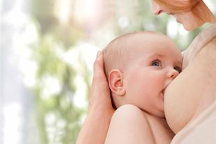 Eine Mutter, die ihr Baby sanft an ihre Brust drückt, wobei das Baby nach oben schaut und die Mutter lächelt.