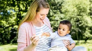 Eine Frau hält ein Baby im Freien, das sie mit einem Löffel füttert.