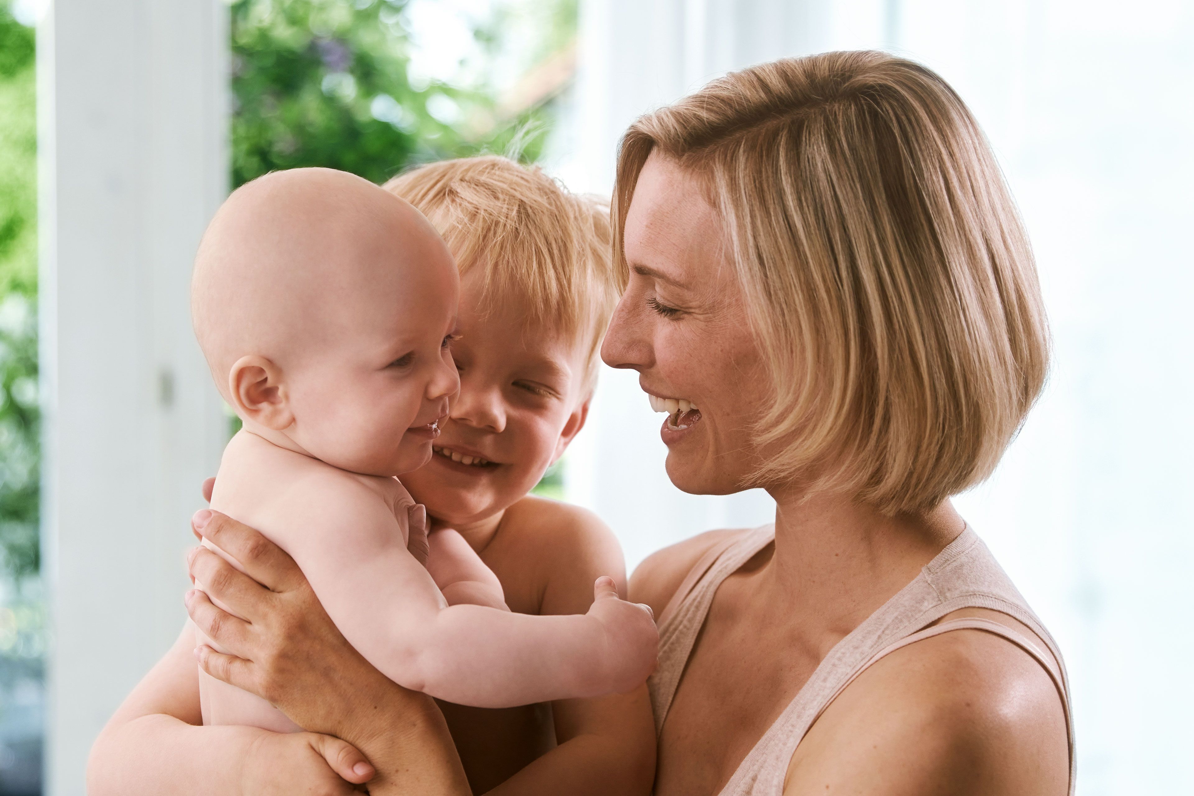 Ein freudiger Moment zwischen einer Mutter und ihren beiden Kindern, wobei die Mutter ein Baby im Arm hält und ein kleiner Junge sie anschaut.