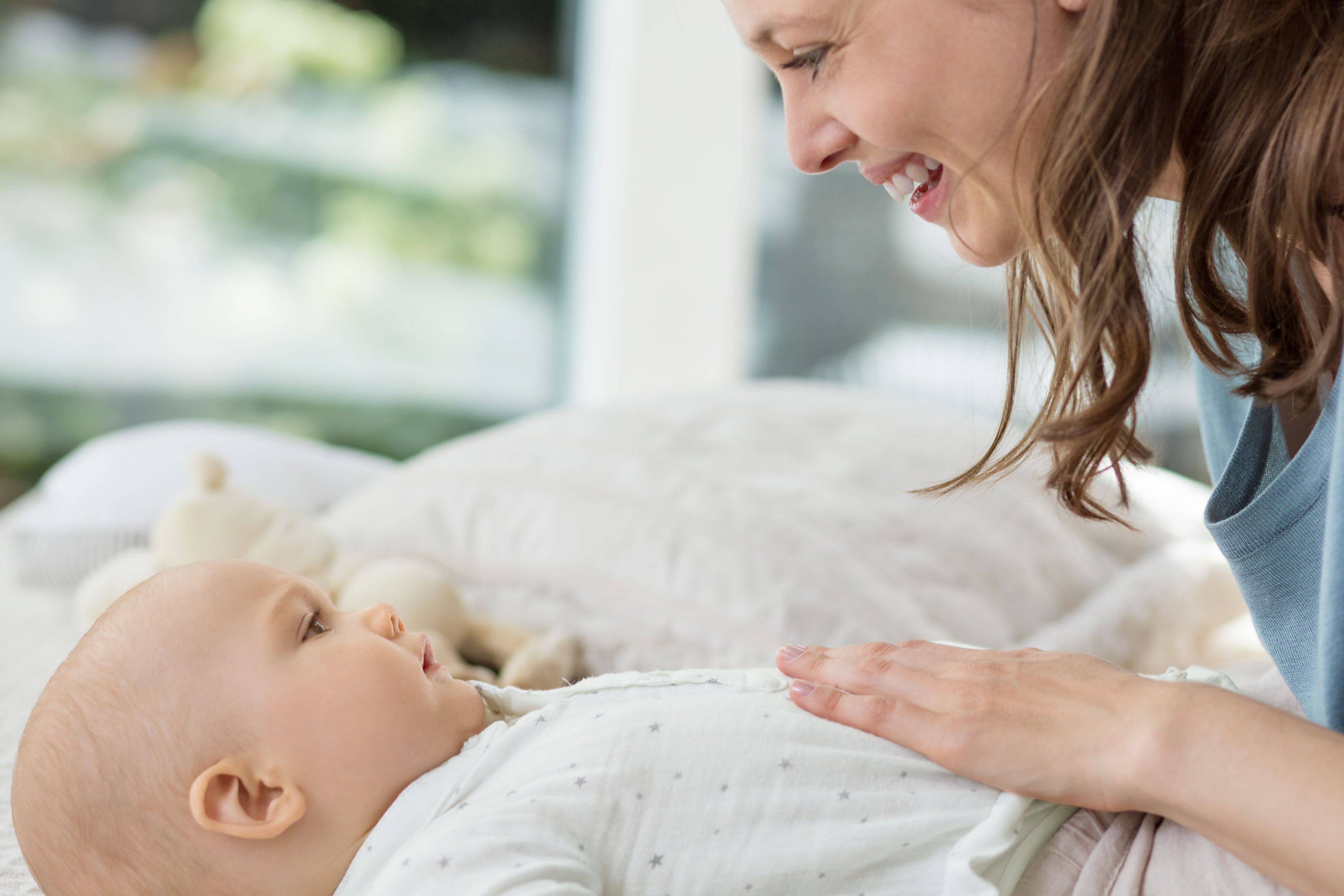 Lächelnde Mutter streichelt sanft den Bauch ihres auf dem Rücken liegenden Babys, um die Verdauung zu unterstützen.