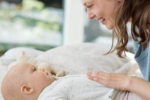 Lächelnde Mutter streichelt sanft den Bauch ihres auf dem Rücken liegenden Babys, um dessen Verdauung zu beruhigen.