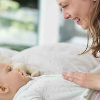 Lächelnde Mutter streichelt sanft den Bauch ihres auf dem Rücken liegenden Babys, um die Verdauung zu unterstützen.