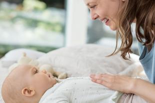 Lächelnde Mutter streichelt sanft den Bauch ihres auf dem Rücken liegenden Babys, um dessen Verdauung zu beruhigen.