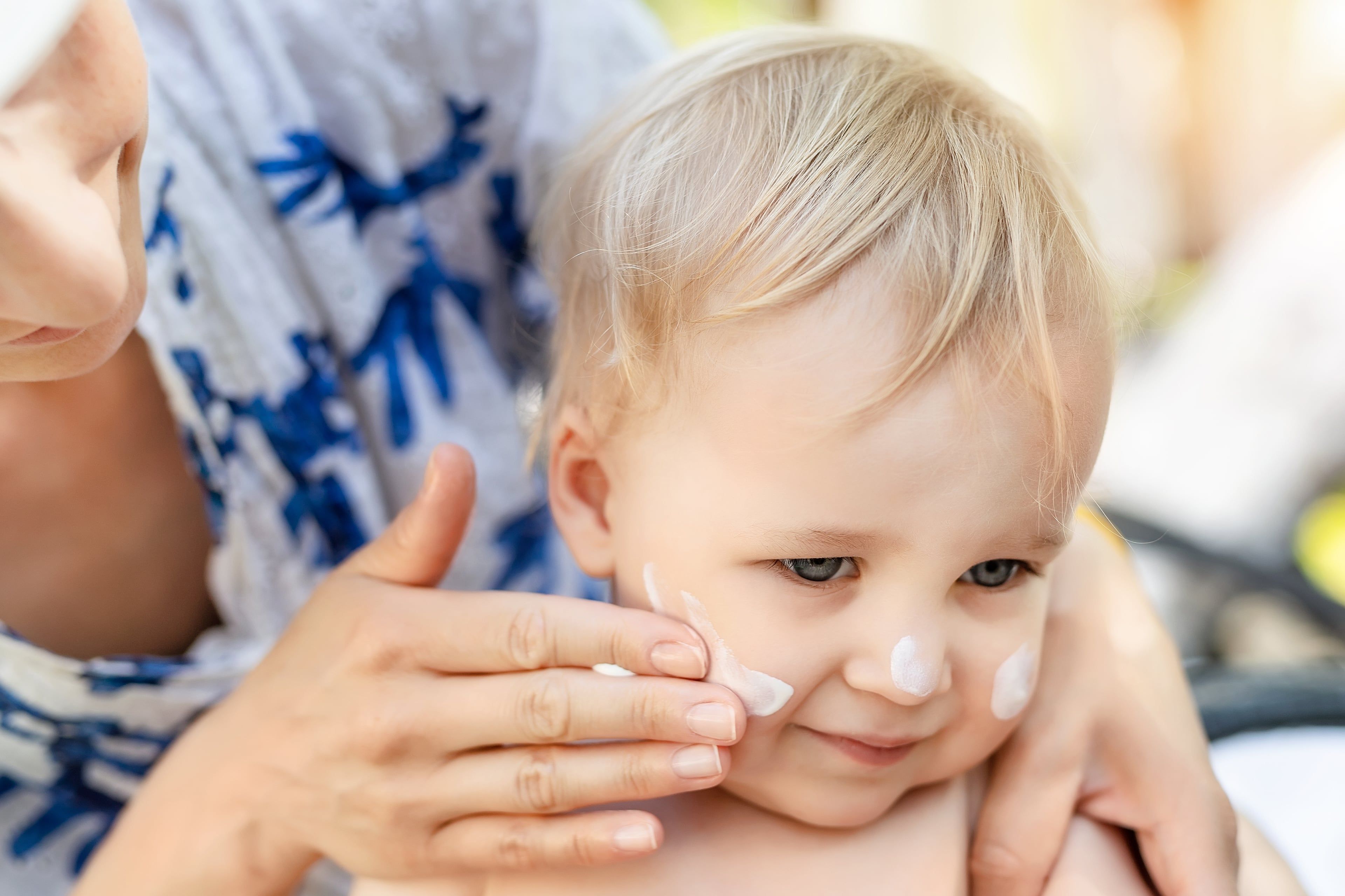 Eine Frau trägt Sonnenschutzmittel auf das Gesicht eines Babys auf.