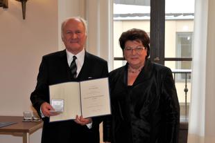 Prof. Dr. Claus Hipp steht mit Landtagspräsidentin Barbara Stamm, hält Urkunde und Etui zur Bayerischen Verfassungsmedaille in Gold.