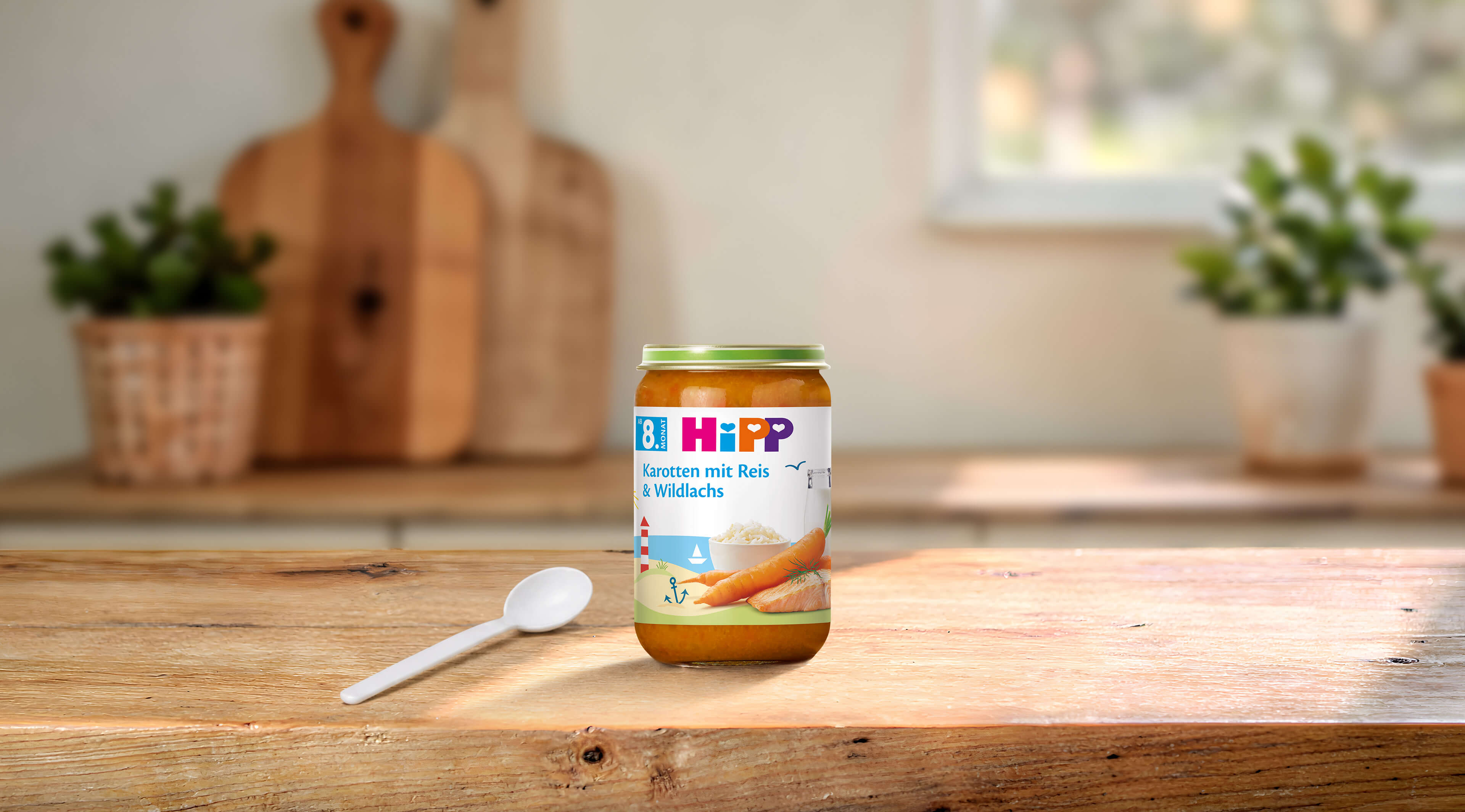 HiPP Bio Babygläschen „Karotten mit Reis & Wildlachs“ ab 8. Monat auf Holztisch mit Löffel in heller Küche