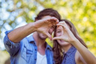 Ein junger Mann und eine junge Frau bilden mit ihren Händen eine Herzform vor einem unscharfen natürlichen Hintergrund.