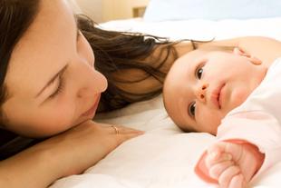 Mutter liegt entspannt neben ihrem wachen Baby im Bett und schenkt ihm Nähe und Ruhe bei Beschwerden rund um den Milcheinschuss