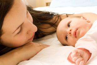 Mutter liegt entspannt neben ihrem wachen Baby im Bett und schenkt ihm Nähe und Ruhe bei Beschwerden rund um den Milcheinschuss