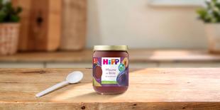 HiPP Bio Babyfruchtglas „Pflaume in Birne“ auf Holztisch mit Löffel, im hellen, gemütlichen Küchenhintergrund