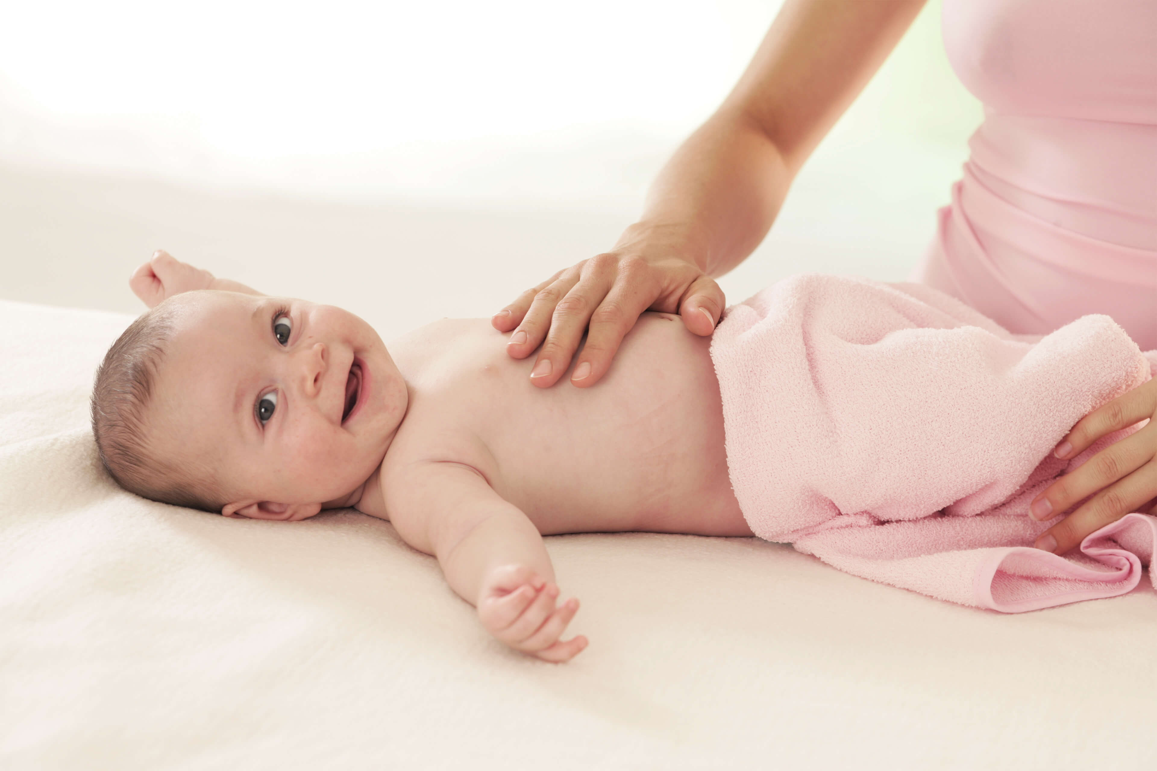 Ein Baby, das ein Plüschtier hält und von einer Erwachsenenhand sanft berührt wird.