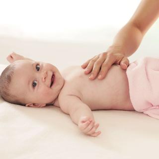Ein Baby, das ein Plüschtier hält und von einer Erwachsenenhand sanft berührt wird.