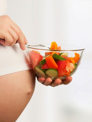 Eine Person hält eine durchsichtige Schüssel mit einem bunten Salat in der Hand, wobei der Schwerpunkt auf dem Mittelteil der Person und den Zutaten des Salats liegt.