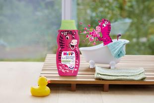 Flasche Haarschampoo mit einem rosa Zebra-Motiv neben einer Badewanne, in der ein kleines Zebra mit Seifenblasen sitzt, davor eine gelbe Gummiente auf einem Holzbrett.
