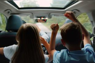 Zwei Kinder, ein Mädchen und ein Junge, sitzen mit erhobenen Händen in einem Auto und scheinen eine Fahrt zu genießen.
