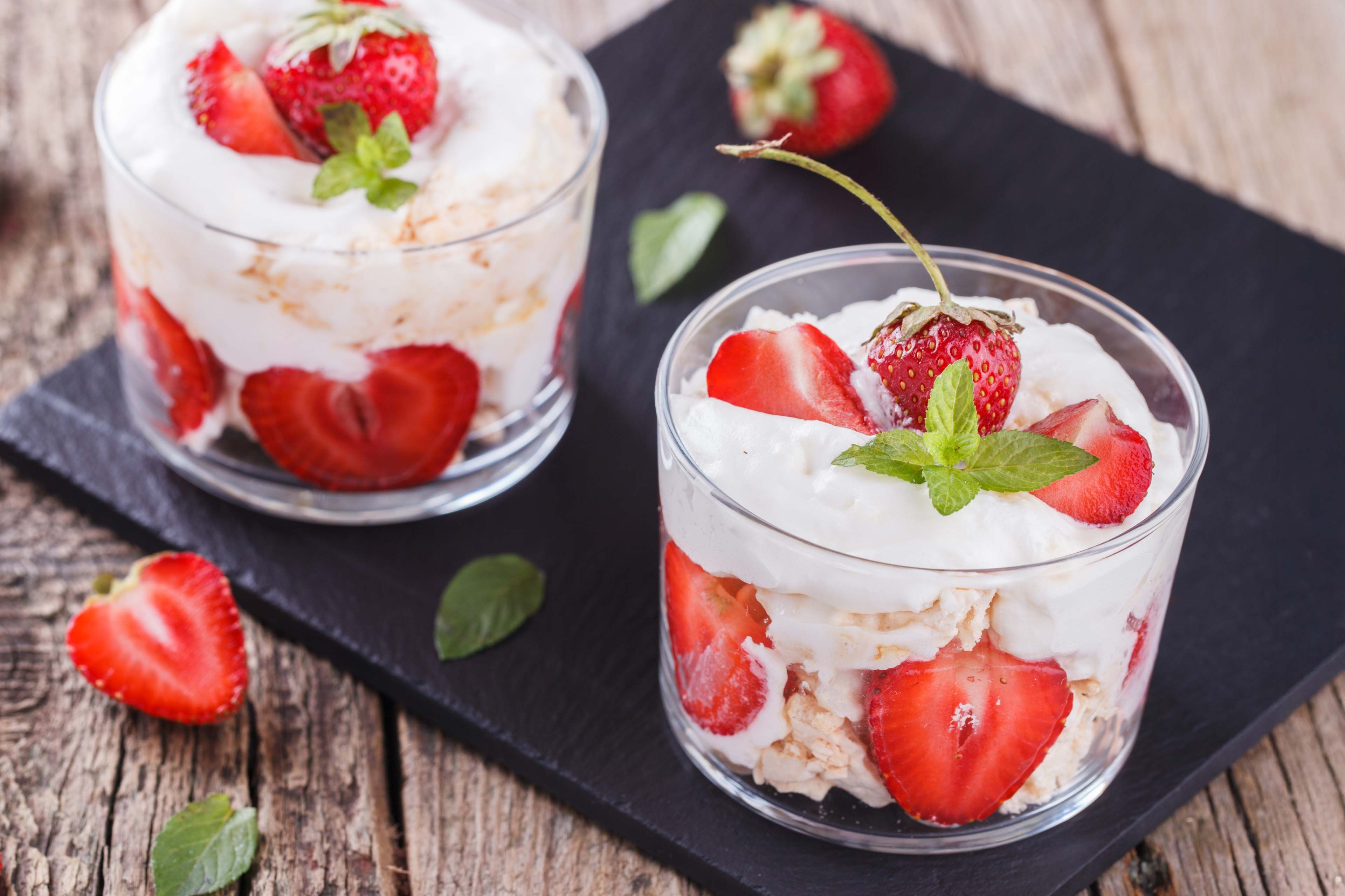 Zwei Gläser, gefüllt mit einem cremigen Dessert, garniert mit frischen Erdbeeren und Minzblättern.
