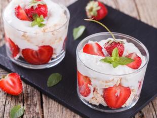 Zwei Gläser, gefüllt mit einem cremigen Dessert, garniert mit frischen Erdbeeren und Minzblättern.