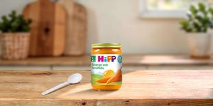 HiPP Bio Babygläschen Karotten mit Kartoffeln auf Holztisch mit Löffel in heller, gemütlicher Küche