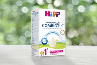 Packung HiPP Kindermilch Combiotik mit natürlicher Milchsäurekultur auf Holztisch vor unscharf grünem Hintergrund