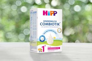 Packung HiPP Kindermilch Combiotik mit natürlicher Milchsäurekultur auf Holztisch vor unscharf grünem Hintergrund