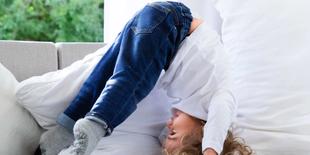 Ein Kind in einem weißen Hemd und einer blauen Jeans, kopfüber auf einer Couch.