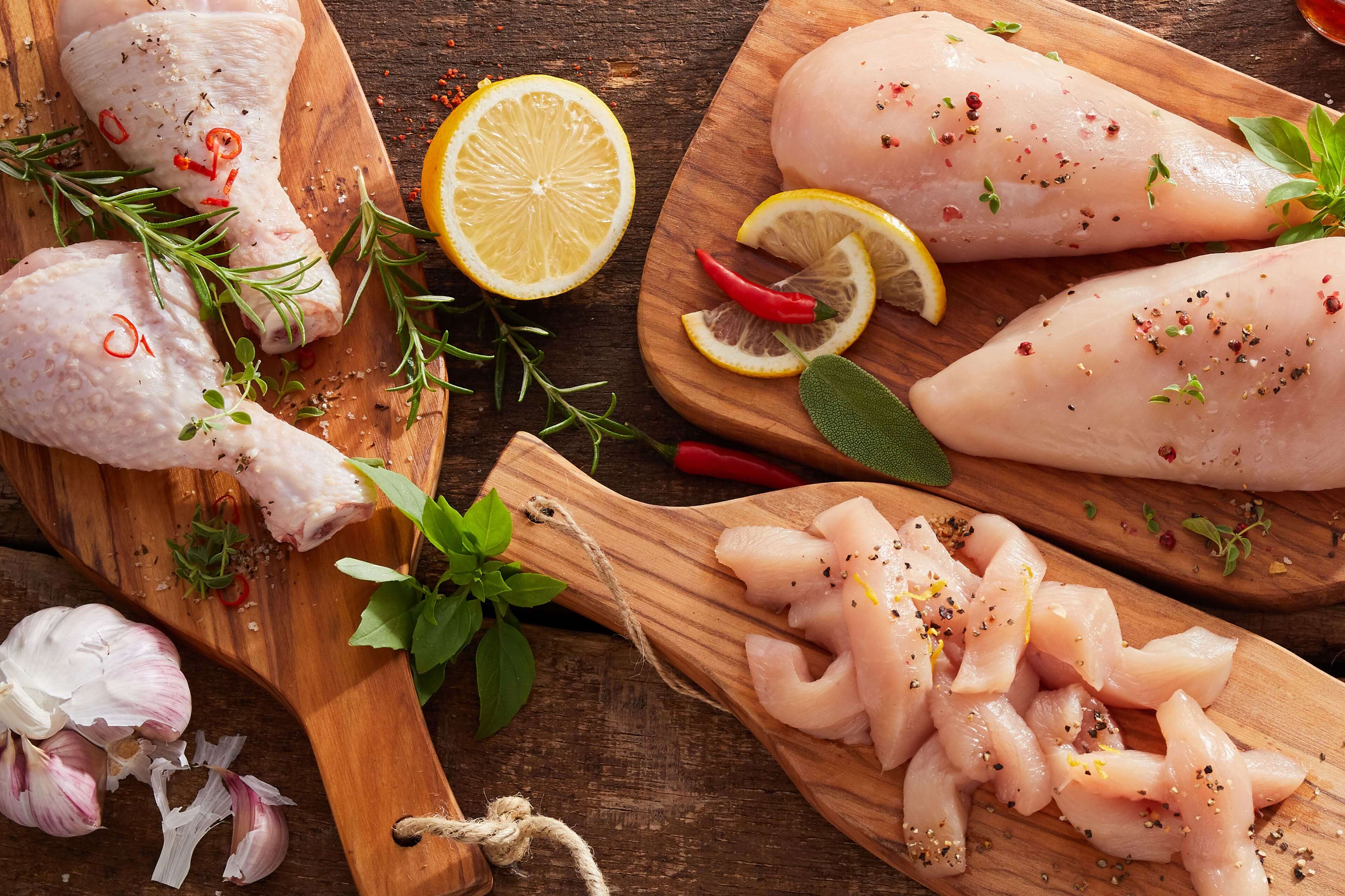 Verschiedene Teile von rohem Hühnerfleisch, gewürzt mit Kräutern und Gewürzen, begleitet von Zitronenscheiben und Chilischoten.