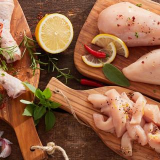 Verschiedene Teile von rohem Hühnerfleisch, gewürzt mit Kräutern und Gewürzen, begleitet von Zitronenscheiben und Chilischoten.
