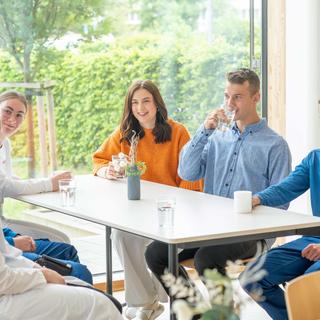 Junge HiPP Mitarbeitende und Auszubildende sitzen entspannt gemeinsam am Tisch und unterhalten sich in einer hellen Kantine.